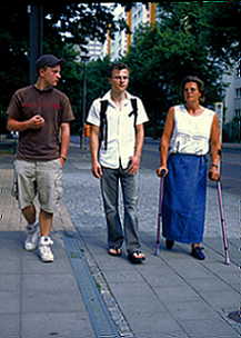 Frau mit St�tzen gehend neben ihren beiden S�hnen auf der Stra�e